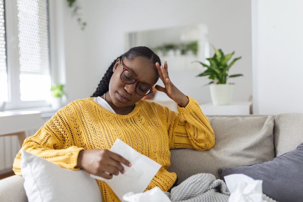 Portrait of an attractive woman sitting on a sofa at home with a headache, feeling pain and with an expression of being unwell. Upset depressed woman lying on couch feeling strong headache migraine.